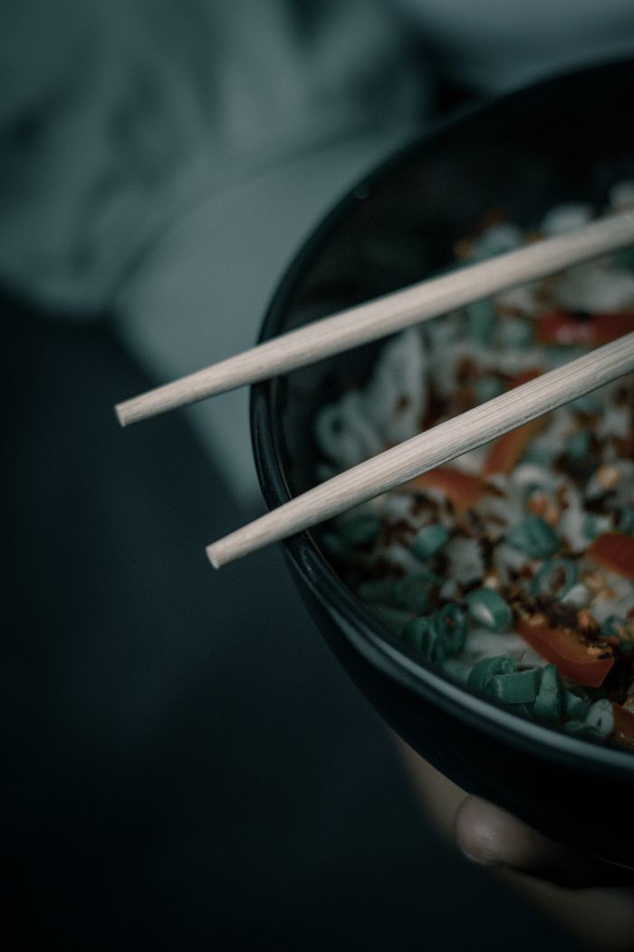 Dark moody close-up of a noodle bowl with chopsticks, perfect for Asian cuisine themes.
